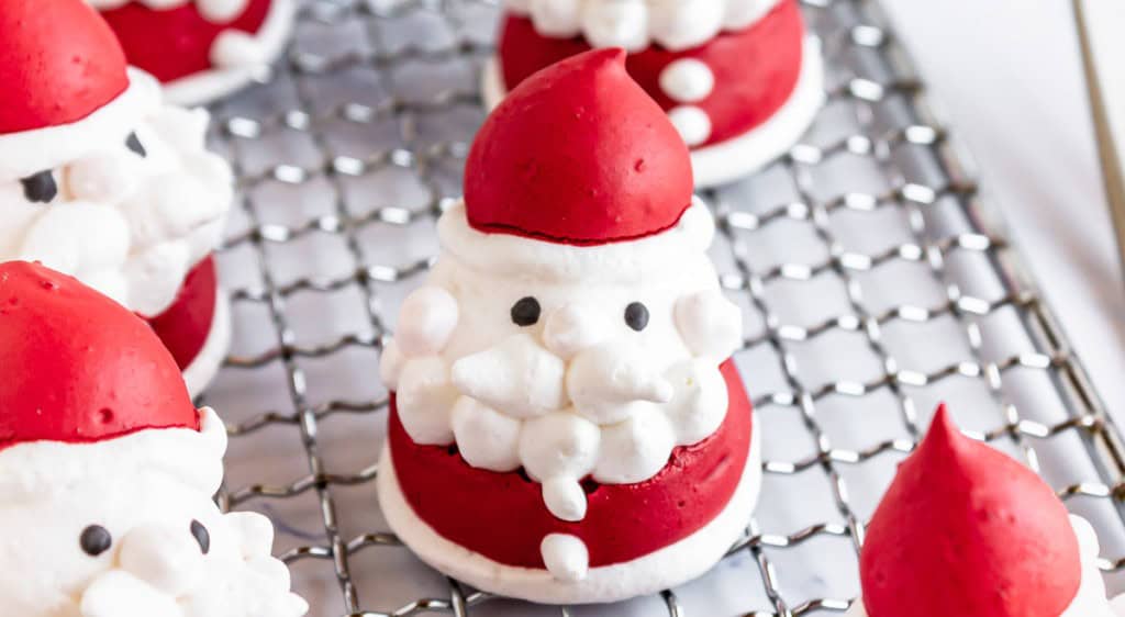 Santa Meringues are a festive treat, with each meringue dessert shaped and decorated to resemble a Santa Claus figure, sitting playfully on a wire cooling rack.