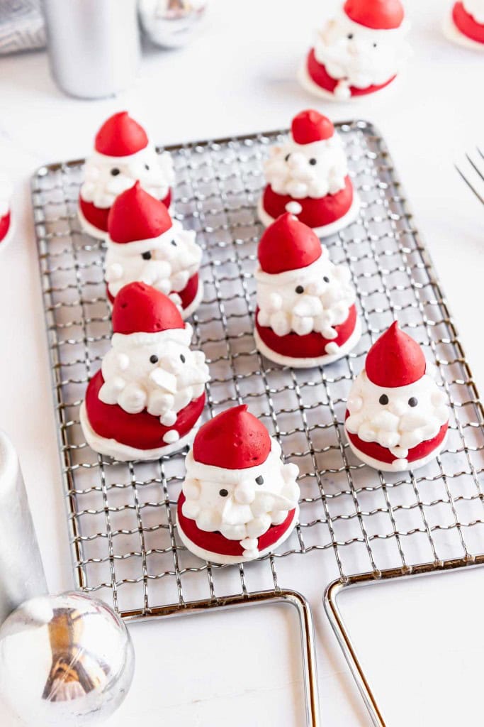 Several Santa Claus-shaped meringue cookies with red hats and white beards are arranged on a cooling rack.