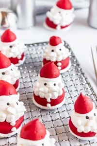 Several Santa Claus-shaped meringue cookies with red hats and white beards are arranged on a cooling rack.