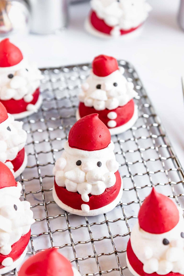Several Santa Claus-shaped meringue cookies with red hats and white beards rest on a wire cooling rack.