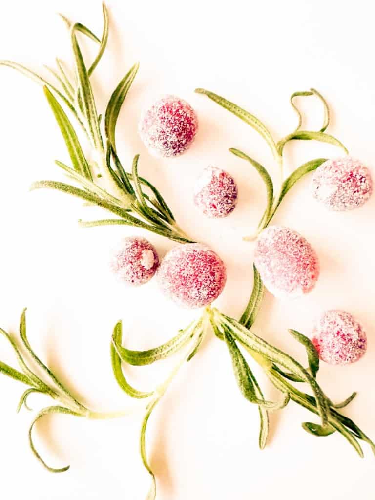 Sugared cranberries and sprigs of rosemary artfully arranged on a white background create a festive, elegant display.