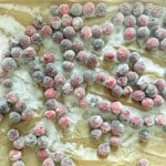 Sugared cranberries spread out on parchment paper, coated evenly with granulated sugar.