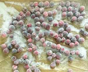 Sugared cranberries spread out on parchment paper, coated evenly with granulated sugar.