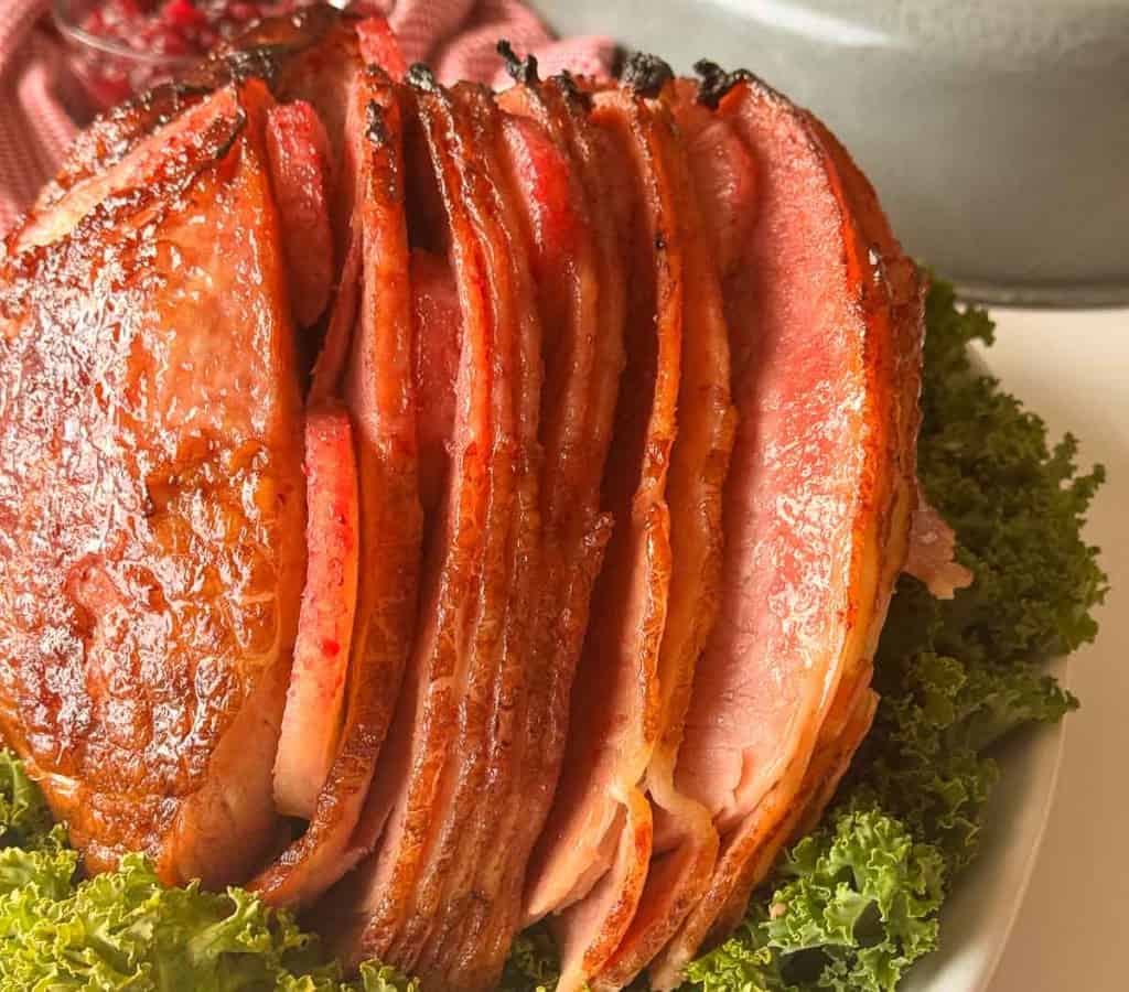 Sliced glazed ham arranged on a bed of leafy green lettuce.