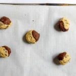Five unbaked, half-chocolate and half-vanilla cookie dough balls on a parchment-lined baking sheet.