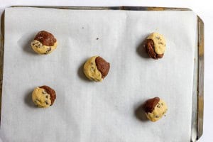 Five unbaked, half-chocolate and half-vanilla cookie dough balls on a parchment-lined baking sheet.