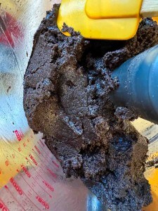 A close-up of thick, dark chocolate dough for Chocolate Pinecone Truffles being mixed in a clear bowl with a yellow spatula.