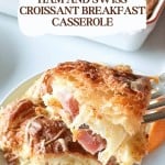A fork holds a bite of ham and Swiss croissant breakfast casserole, with the golden casserole dish in the background. Text overlay reads: "Ham and Swiss Croissant Breakfast Casserole." Perfect for brunch!.