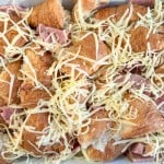Chopped croissants topped with ham and Swiss, shredded cheese, and pieces of ham in a baking dish create a delicious ham and swiss croissant breakfast casserole.