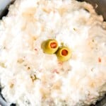 A bowl of creamy cottage cheese salad topped with three green olives, placed on a striped cloth.