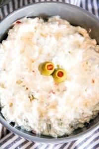 A bowl of creamy cottage cheese salad topped with three green olives, placed on a striped cloth.