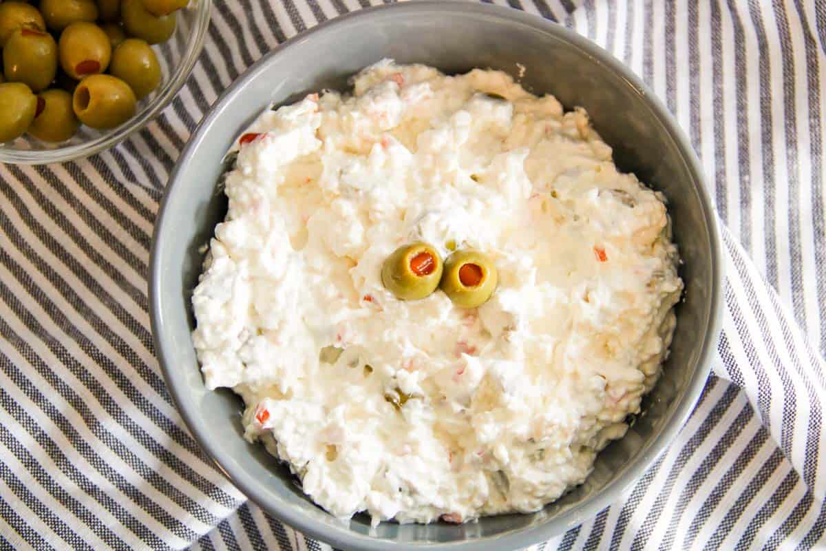 Creamy olive dip in a gray bowl topped with two green olives, set on a striped cloth.