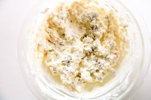 A glass bowl containing a creamy mixture with visible chunks of fruit and nuts, possibly a fruit salad or dessert.
