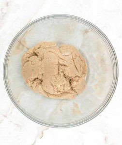 A ball of cookie dough sits in a clear glass mixing bowl on a white marble surface.