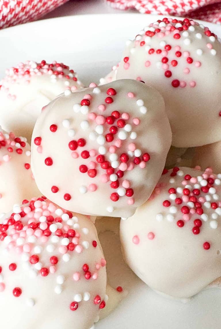 White chocolate truffles topped with red, pink, and white sprinkles are arranged on a white plate.