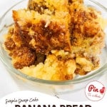 A close-up of banana bread dump cake pieces in a clear glass bowl on a white surface, with website branding and a "Pin to Make" graphic overlay.