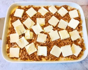 A baking dish filled with an unbaked dessert, topped with crumbled brown sugar and evenly spaced slices of butter.
