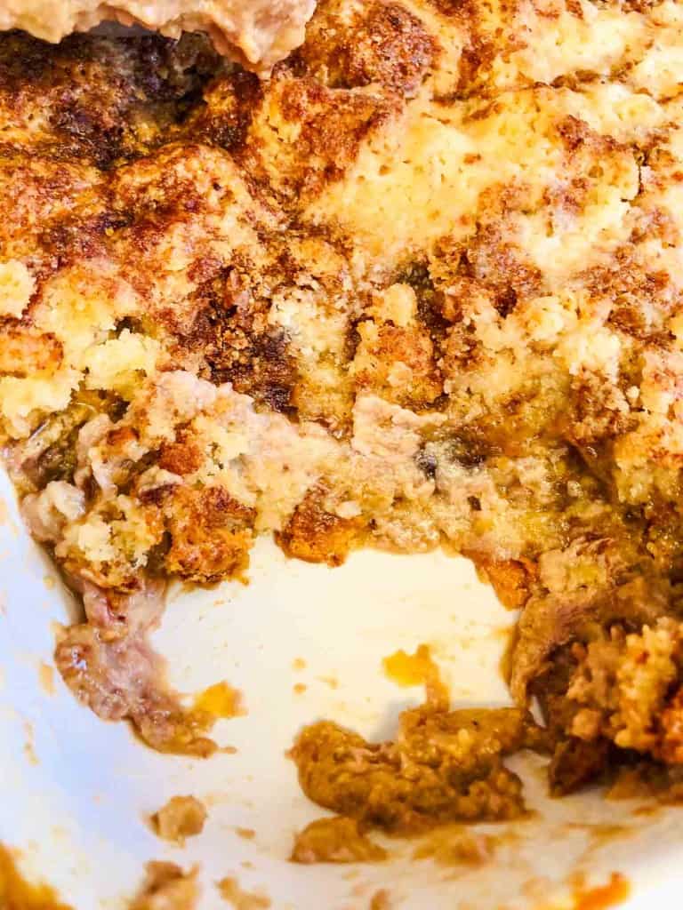 Close-up of a partially eaten baked dessert with a golden-brown, crumbly topping and a gooey filling in a white dish.