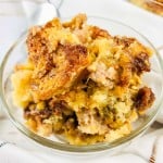A glass bowl filled with a serving of bread pudding featuring a golden-brown, crumbly top on a white cloth.