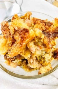 A close-up of a serving of golden-brown, crumbly casserole in a clear glass bowl, placed on a white surface.