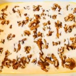 A baking dish filled with a creamy liquid mixture topped with scattered walnut pieces.