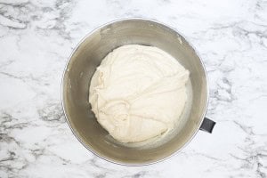 A metal mixing bowl containing smooth, light-colored dough sits on a white marble countertop.