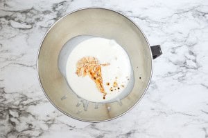 A metal mixing bowl on a marble surface contains cream, peanut butter, and vanilla extract.