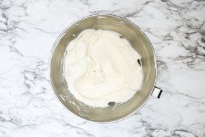 A metal mixing bowl filled with smooth, creamy white batter sits on a marble countertop.