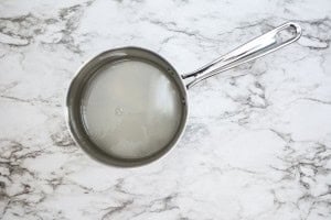 A stainless steel saucepan filled with clear liquid sits on a white marble countertop.