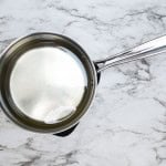 A stainless steel saucepan filled with clear water sits on a marble countertop.