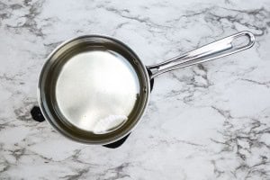 A stainless steel saucepan filled with clear water sits on a marble countertop.
