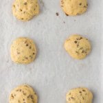 Six round chocolate chip cookies spaced evenly on a parchment-lined baking sheet.