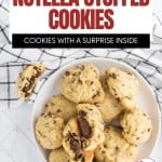 A bowl of nutella stuffed cookies, some broken open to reveal their gooey center, sits on a white surface next to a black-and-white checkered cloth.