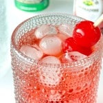 A textured glass filled with ice and red liquid, garnished with two maraschino cherries on a cocktail pick.