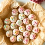 A plate lined with parchment paper holds round white chocolate-coated cake balls topped with colorful sprinkles and red sugar crystals—perfect Valentine's Day treats.