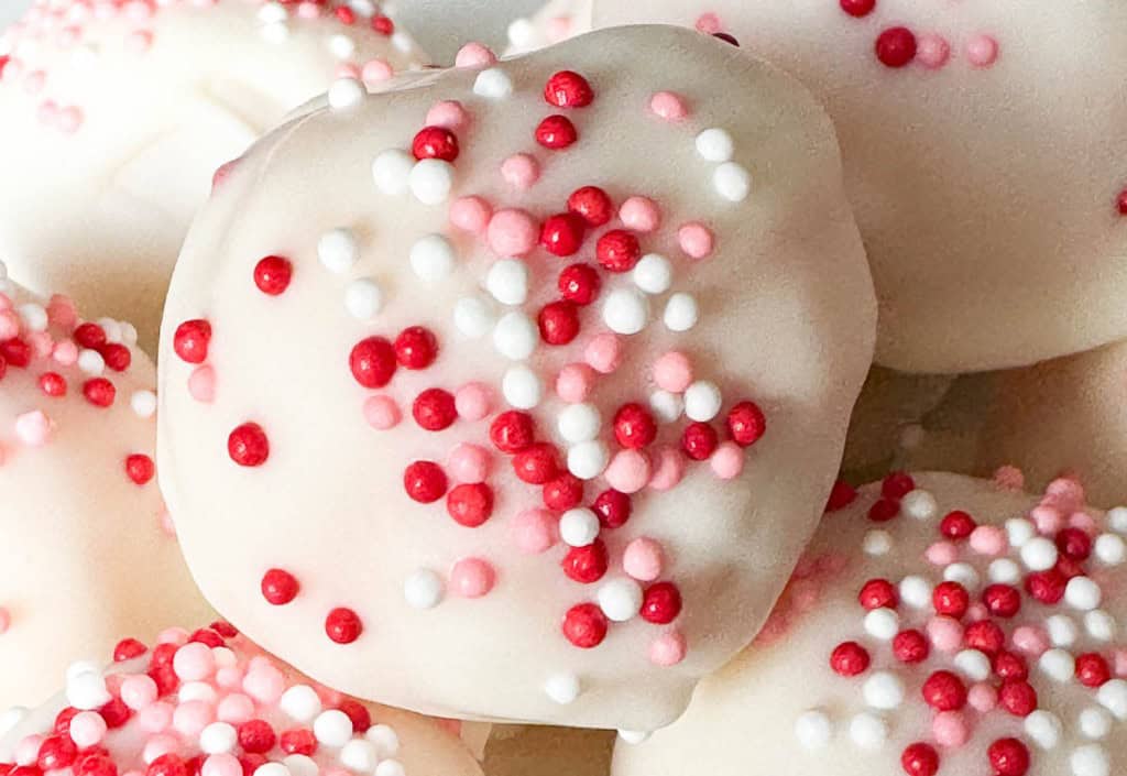 Close-up of a white chocolate covered treat topped with red, pink, and white round sprinkles—perfect for Valentine's Day Treats.
