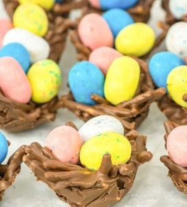 Chocolate nests filled with pastel-colored candy eggs are arranged on a white surface.