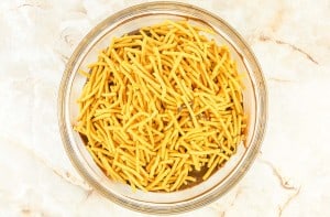 A clear glass bowl filled with crispy, golden-yellow fried potato sticks on a light marble surface.