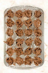 A metal muffin tin lined with plastic wrap contains clusters of chocolate-covered stick-shaped snacks, arranged in each section.