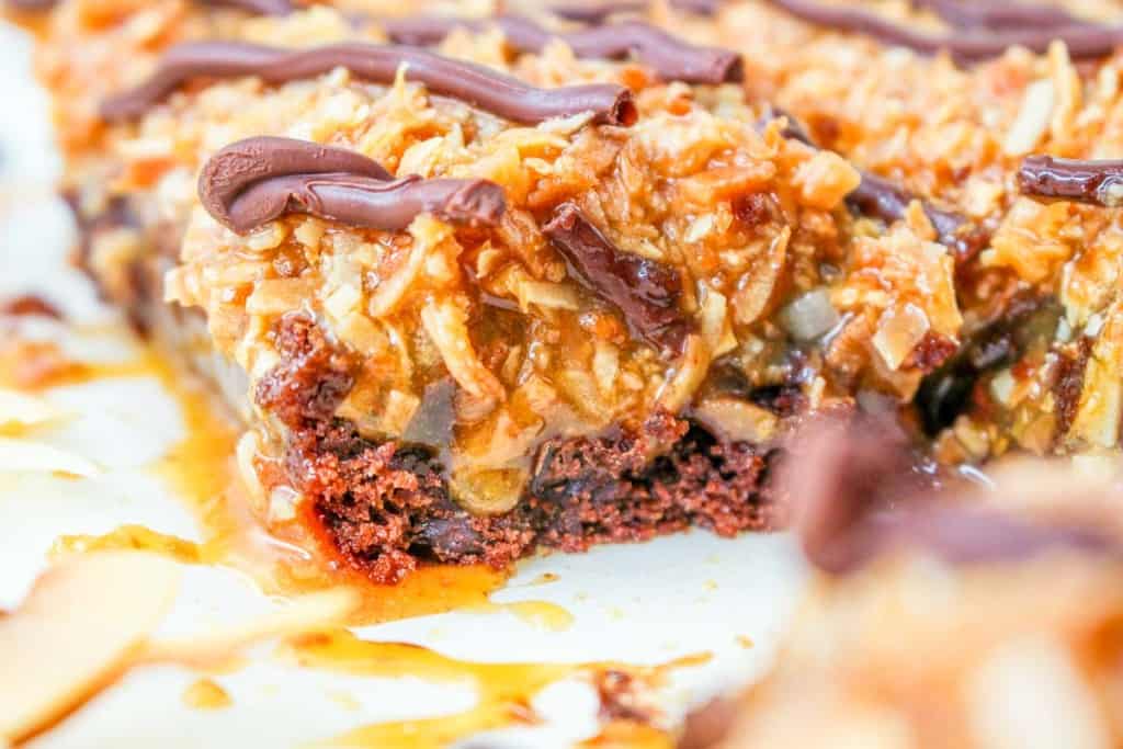 Close-up of a dessert bar with a chocolate base, caramel layer, toasted coconut topping, and drizzled chocolate.