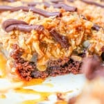 Close-up of a dessert bar with a chocolate base, caramel layer, toasted coconut topping, and drizzled chocolate.
