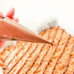 A hand holds a piping bag filled with chocolate, drizzling it in lines over a tray of baked dessert.