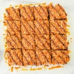 A batch of sixteen caramel coconut bars with chocolate drizzle, arranged in a grid on parchment paper.