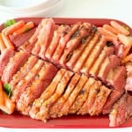 Sliced corned beef arranged on a red platter, garnished with baby carrots and fresh parsley.