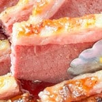Close-up of sliced, cooked slow cooker corned beef with browned edges, shown with metal tongs.