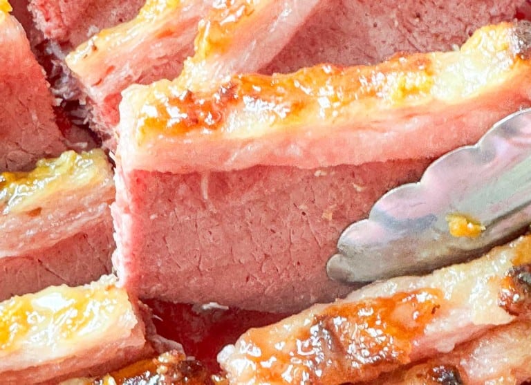 Close-up of sliced, cooked slow cooker corned beef with browned edges, shown with metal tongs.