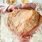 A large piece of raw meat with a layer of fat sits on aluminum foil, with bowls of brown sugar and mustard nearby.