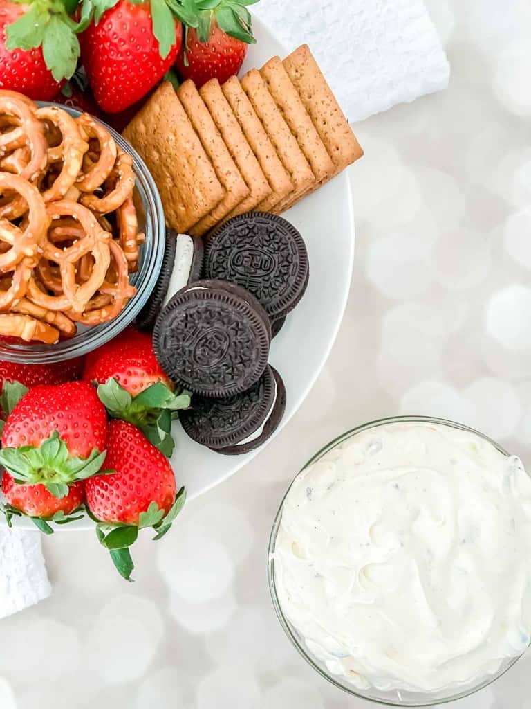 A plate with strawberries, pretzels, graham crackers, and chocolate sandwich cookies next to a bowl of creamy dip.