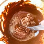 A close-up of melted chocolate being stirred in a glass bowl with a spoon, perfect for making crunchy peanut butter eggs.