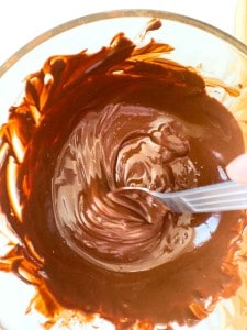 A close-up of melted chocolate being stirred in a glass bowl with a spoon, perfect for making crunchy peanut butter eggs.